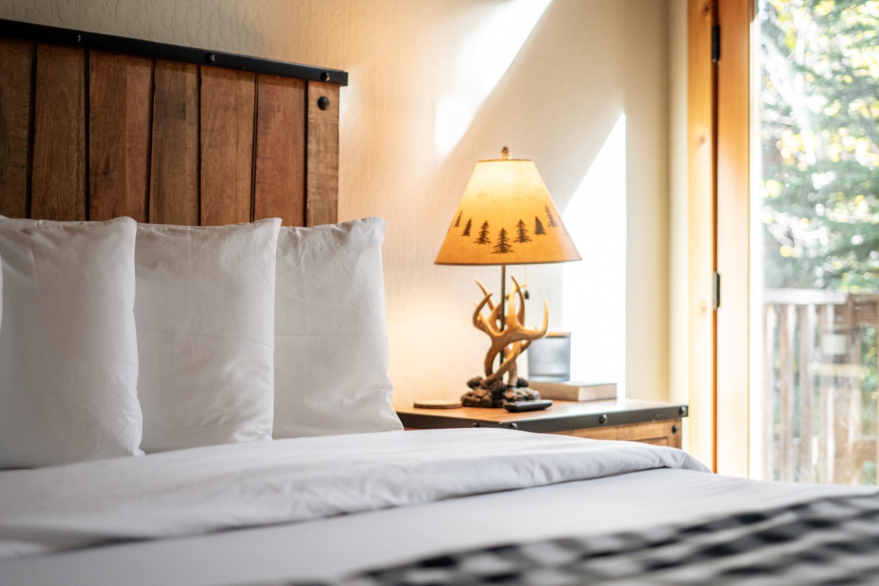 Cozy bedroom in a Truckee vacation rental featuring a rustic wooden bed, white pillows, and a nature-themed lamp.