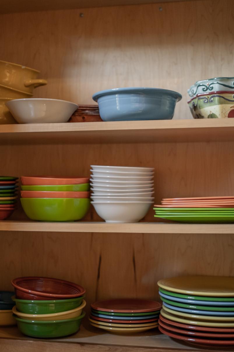 Colorful kitchen bowls and plates neatly stacked on wooden shelves in a Truckee vacation rental.