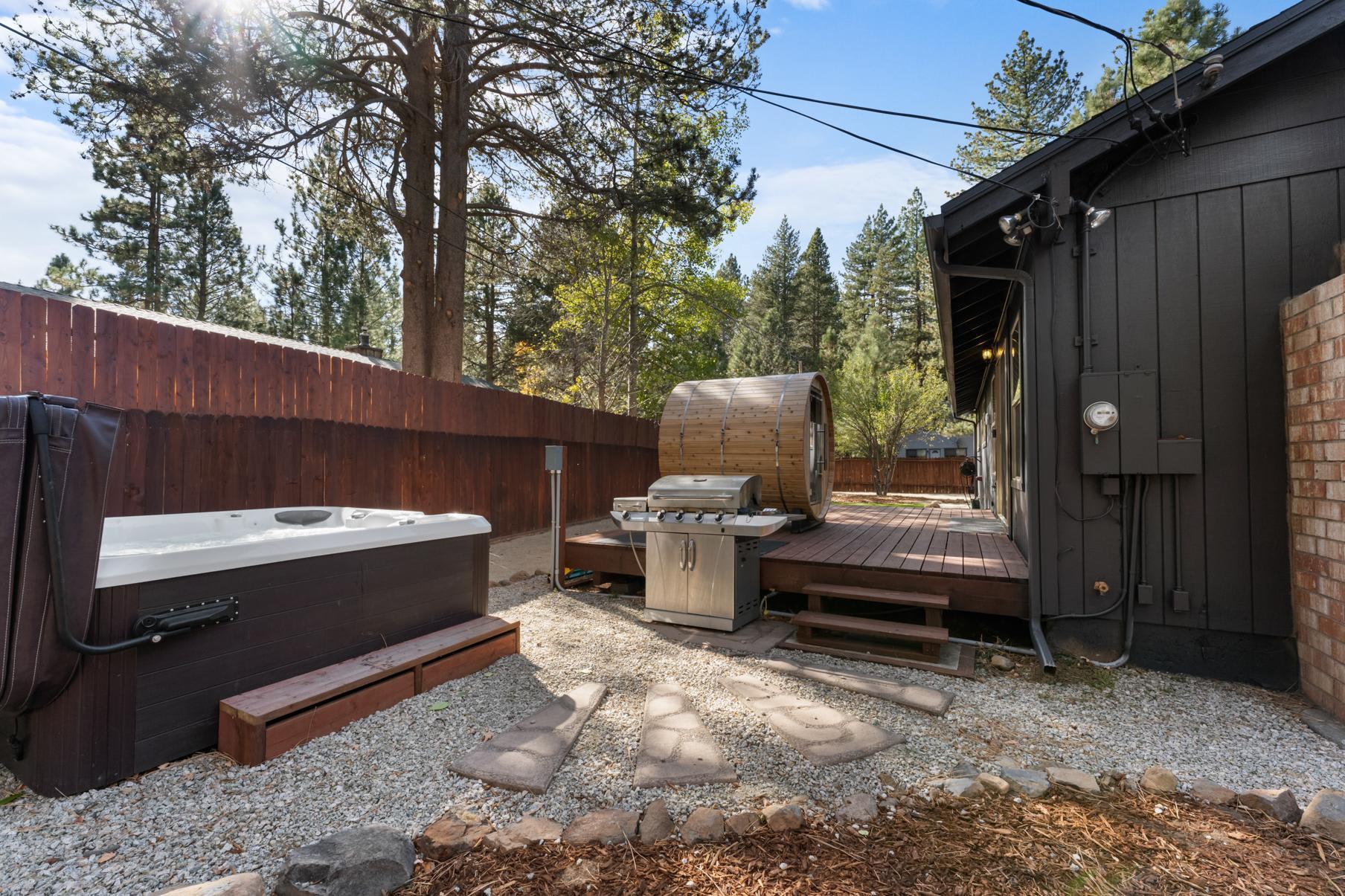 Outdoor deck in Truckee vacation rental with hot tub, sauna, and grill, surrounded by trees and wooden fence.