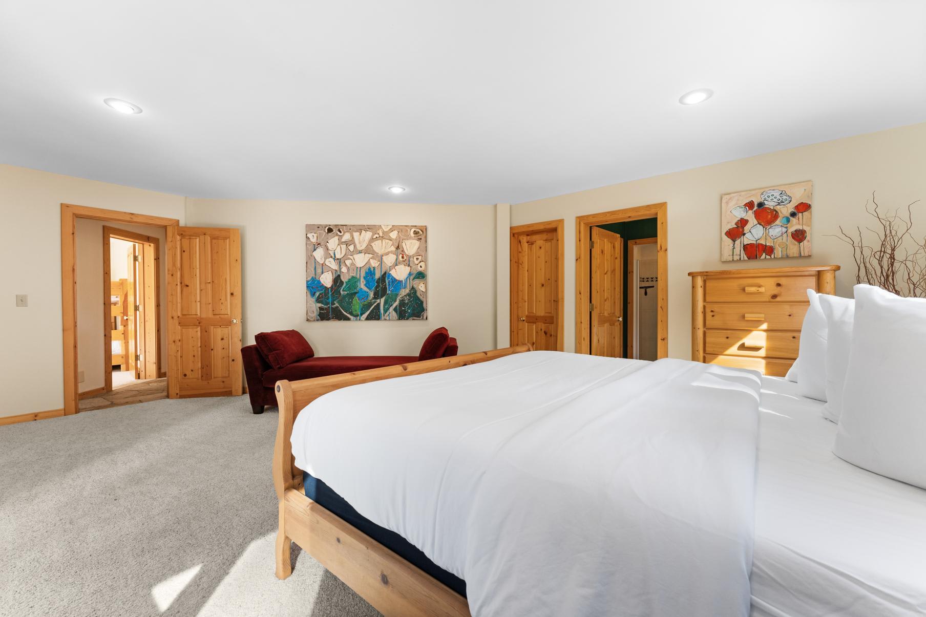 Bright bedroom in a Truckee vacation rental with wood furniture, a large bed, cozy chaise lounge, and nature-themed artwork.