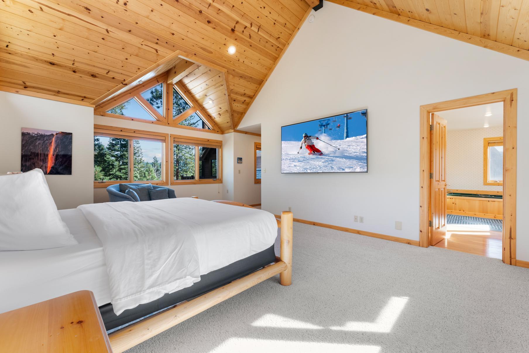 Luxurious bedroom in a Truckee vacation rental, featuring wooden ceilings, a plush bed, and scenic forest views.