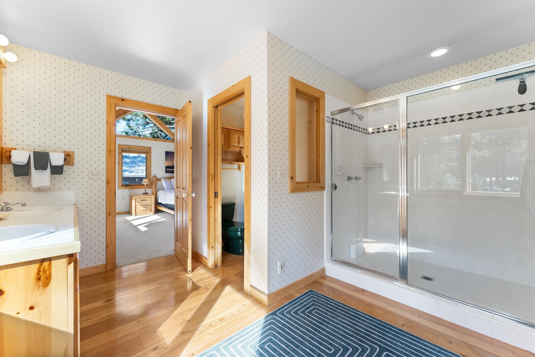 Spacious bathroom in a Truckee vacation rental featuring wooden accents, a glass shower, and a view into a cozy bedroom.