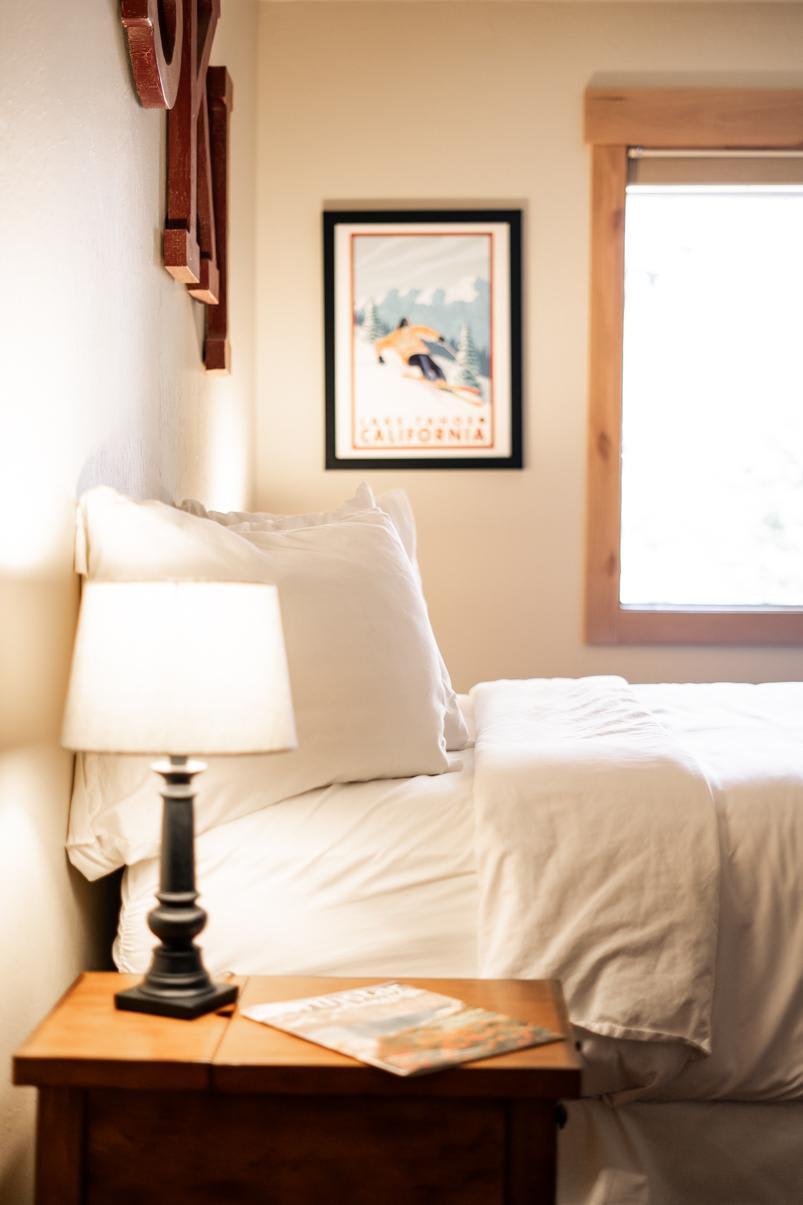 Cozy bedroom in a Truckee vacation rental, featuring a neatly made bed, lamp, and Tahoe poster on the wall.