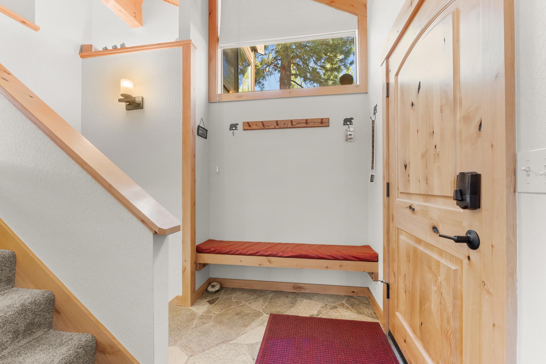 Entrance of a Truckee vacation rental with a wooden bench, stone floor, and stairway, warmly lit with natural wood accents.