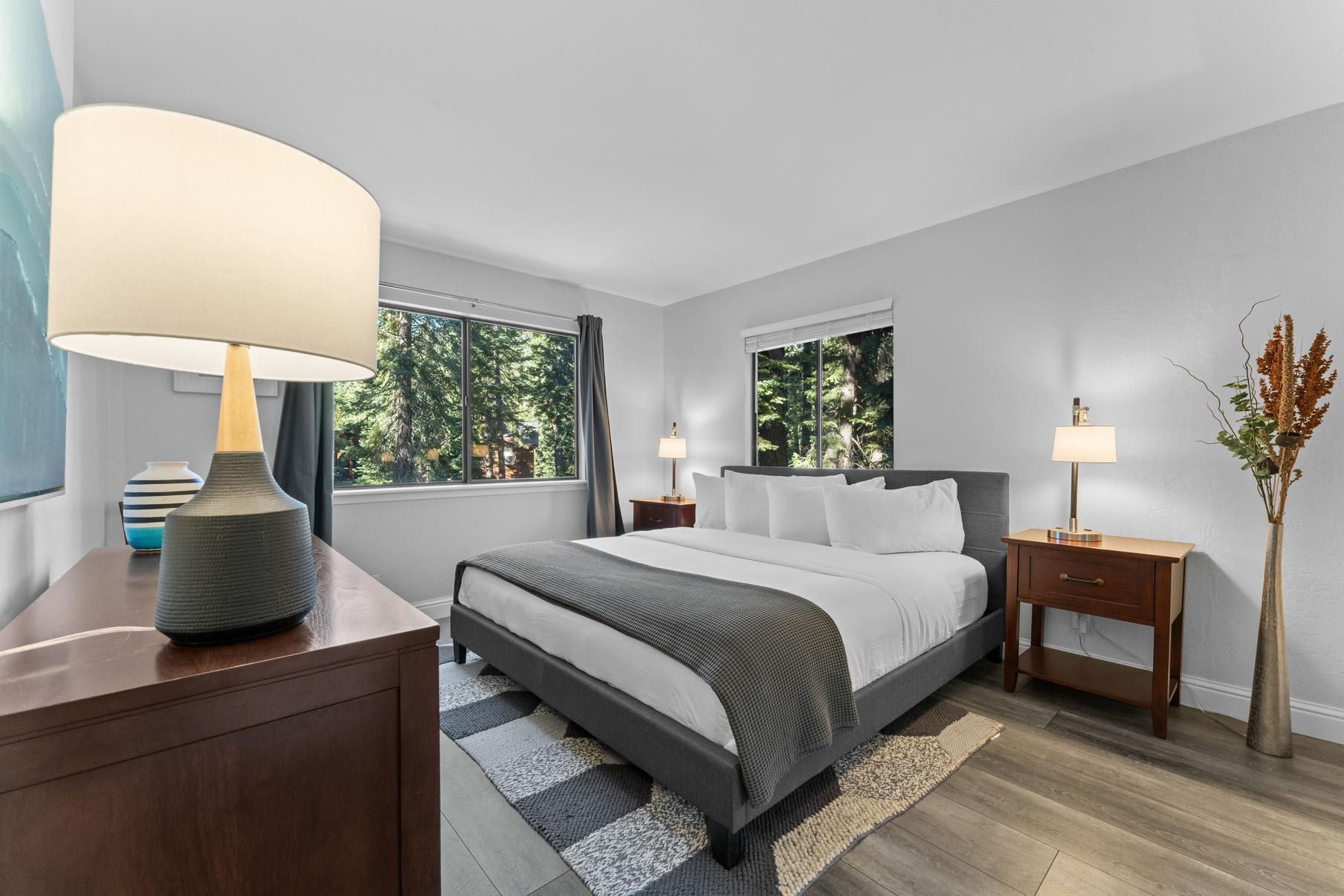 Modern bedroom interior with large bed and windows in a Tahoe Vista vacation rental, featuring forest views.