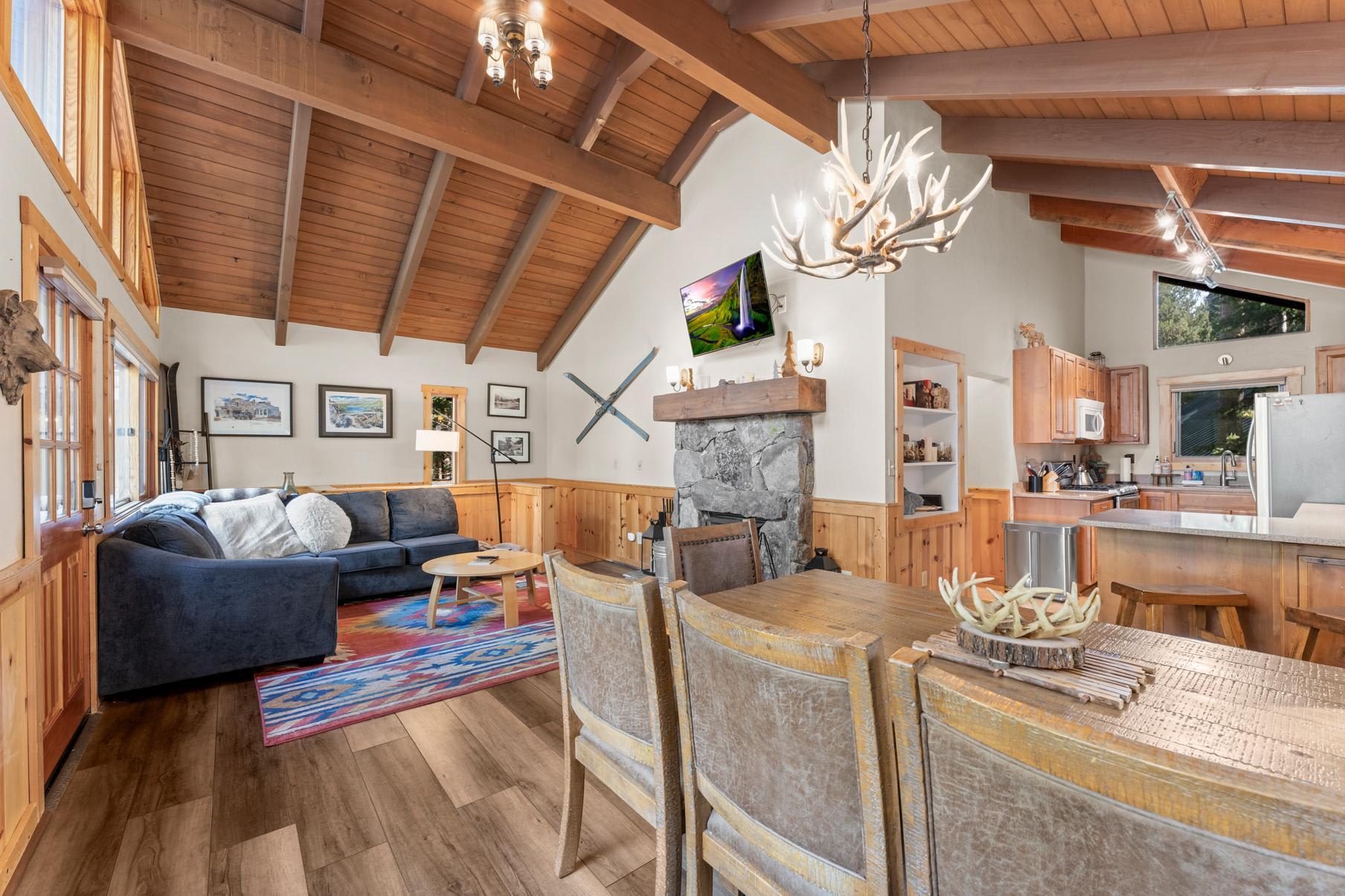 Cozy living area in a Truckee vacation rental, featuring a wooden beamed ceiling, stone fireplace, and modern kitchen.