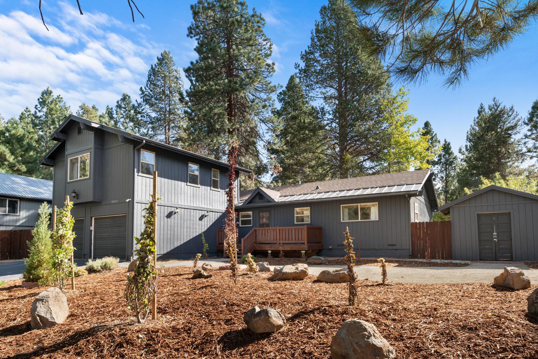 Gray cabin-style vacation rental in Truckee with a wooden deck, surrounded by pine trees and landscaped yard.