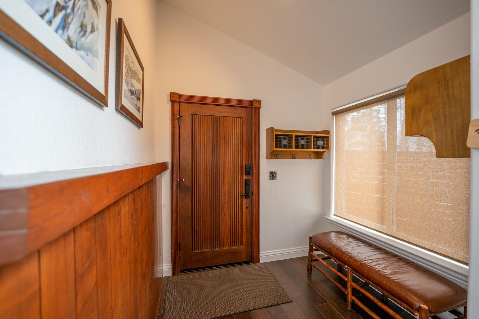 Entrance of a Truckee vacation rental with wooden door, bench, and wall art, offering a cozy and inviting atmosphere.