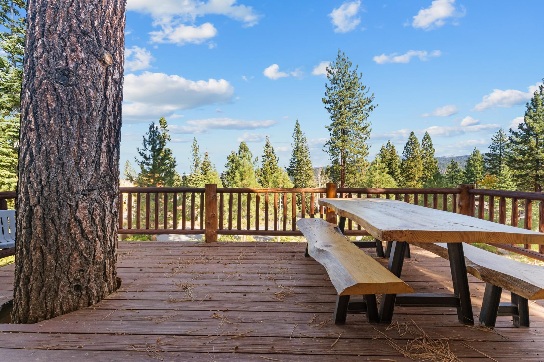 Deck of a Truckee vacation rental with wooden picnic table, surrounded by pine trees and a sunny, blue sky.