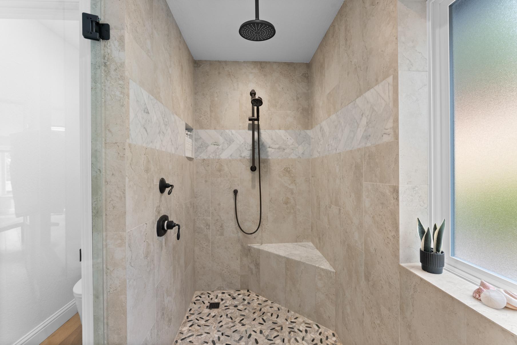 Modern shower in a Truckee vacation rental with beige tiles, black fixtures, and a frosted window with a small potted plant.