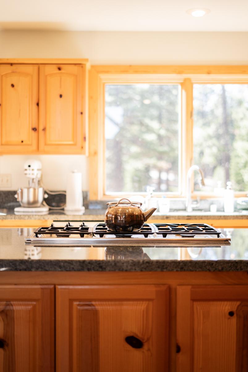 Cozy kitchen in a Truckee vacation rental, featuring wooden cabinets and a stove with a teapot, with a view outside.