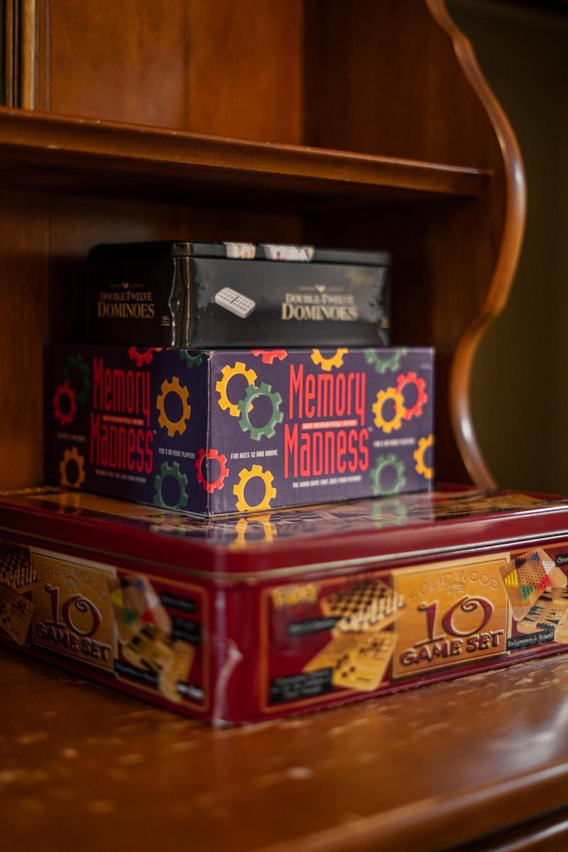 Board games stacked on a wooden shelf in a Truckee vacation rental, featuring Memory Madness and dominoes.