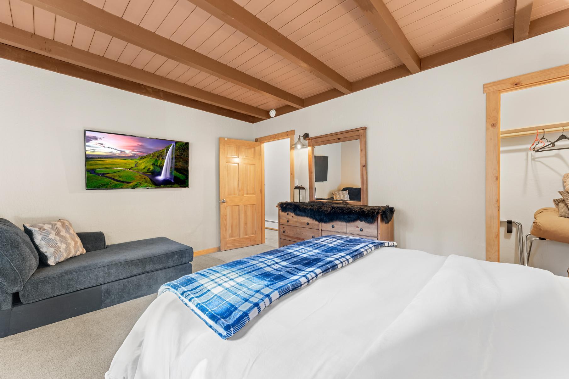 Cozy bedroom in Truckee vacation rental, featuring a bed with blue plaid blanket, TV, sofa, and wooden dresser.