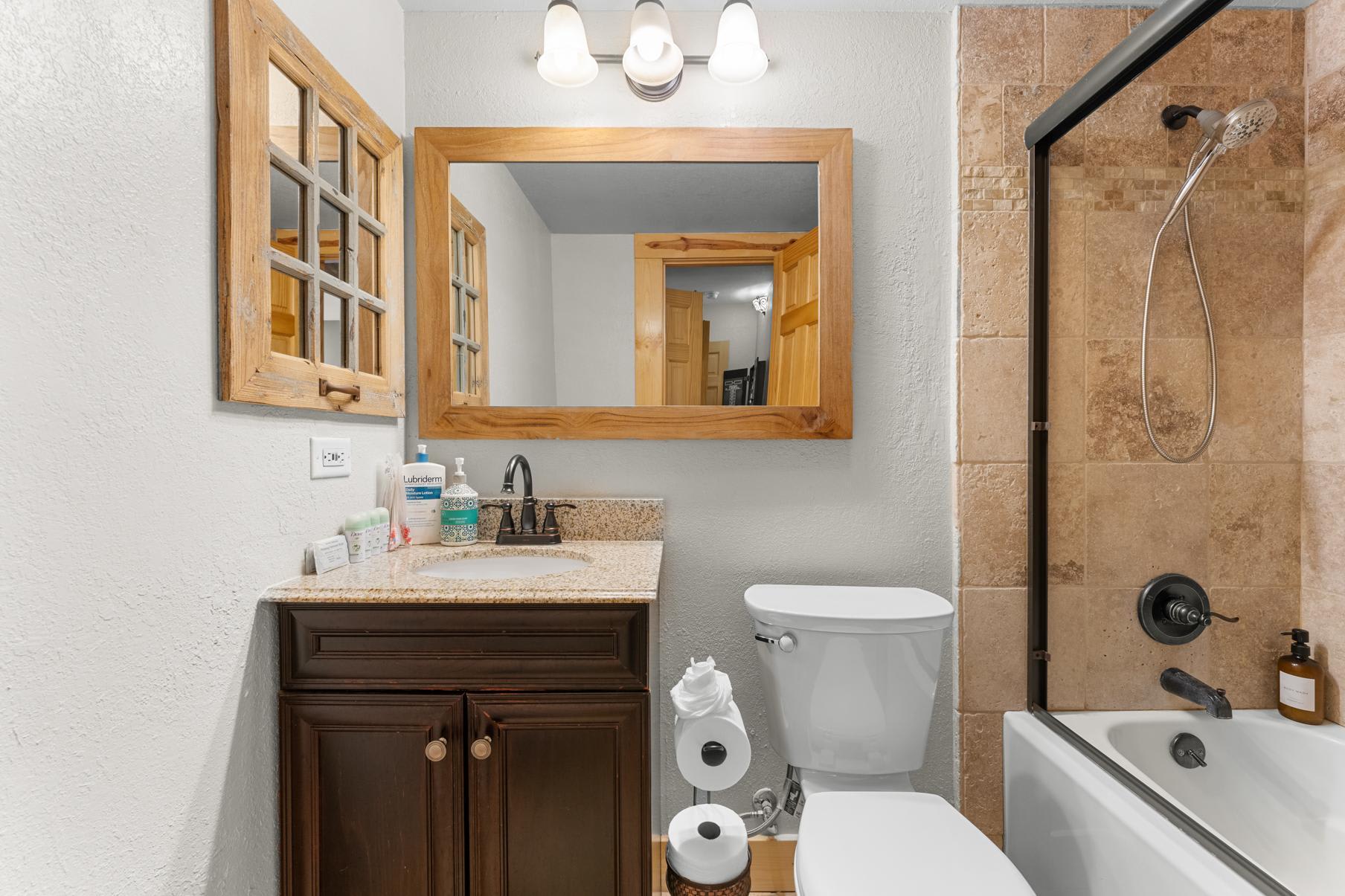 Bathroom in a Truckee vacation rental with a wooden mirror frame, granite countertop, and tiled shower.