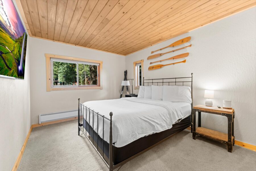 Cozy bedroom in Truckee vacation rental with a wooden ceiling, metal bed, oar decorations, and a forest view.