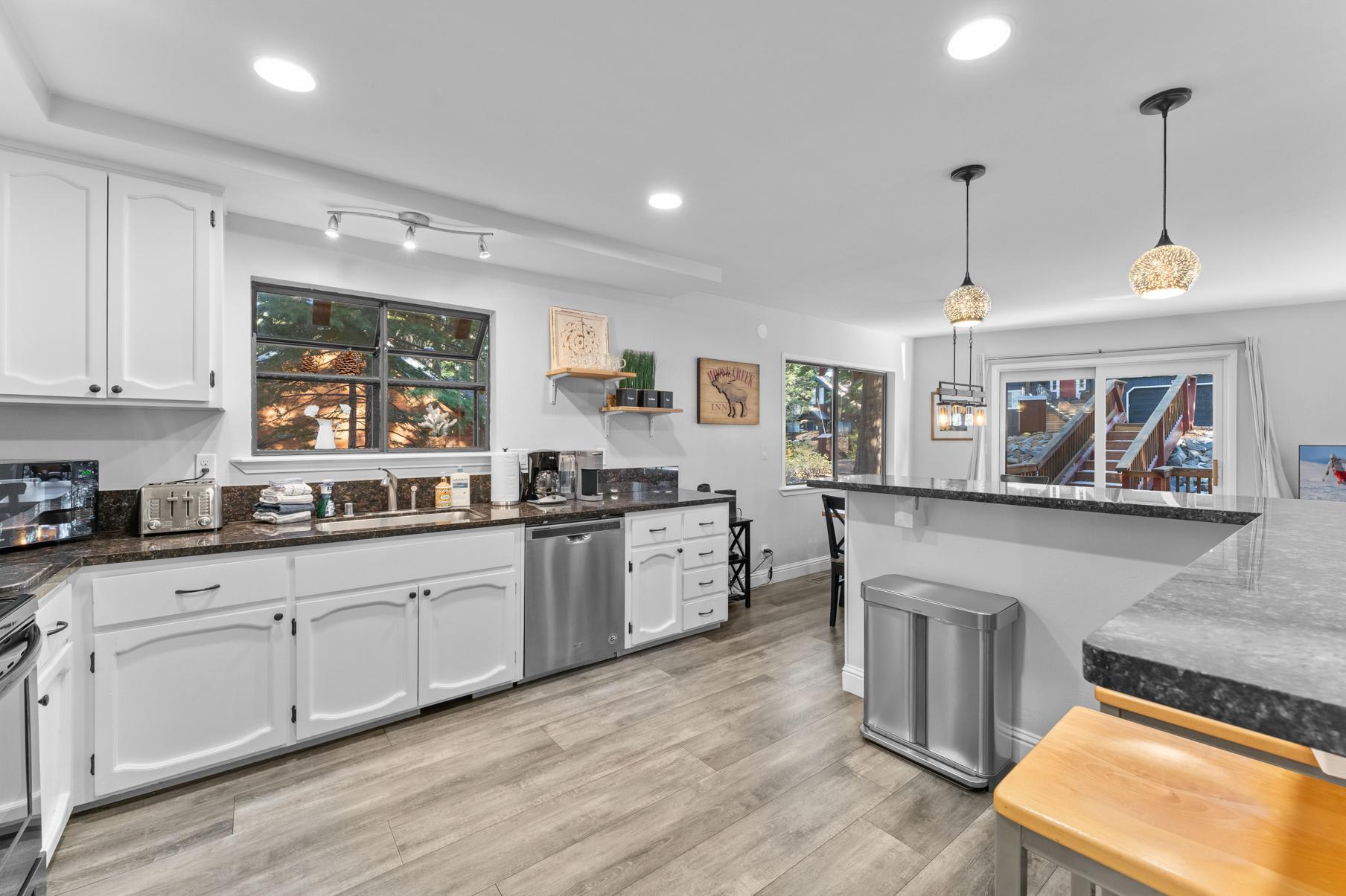 Modern kitchen in a Tahoe Vista vacation rental, featuring white cabinets, bar seating, and large windows.