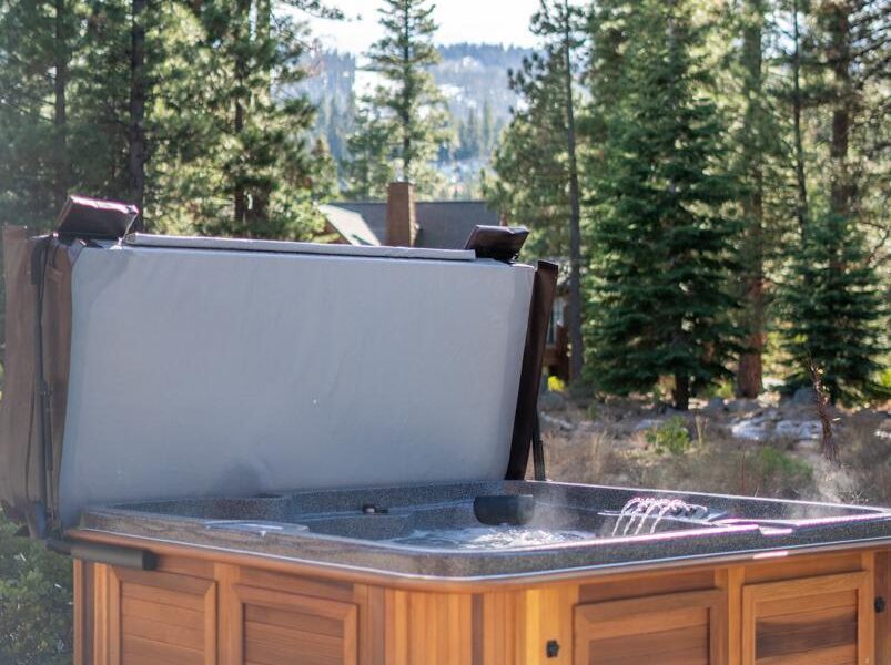 Hot tub on the patio of a Truckee vacation rental, surrounded by tall pine trees and mountain scenery.