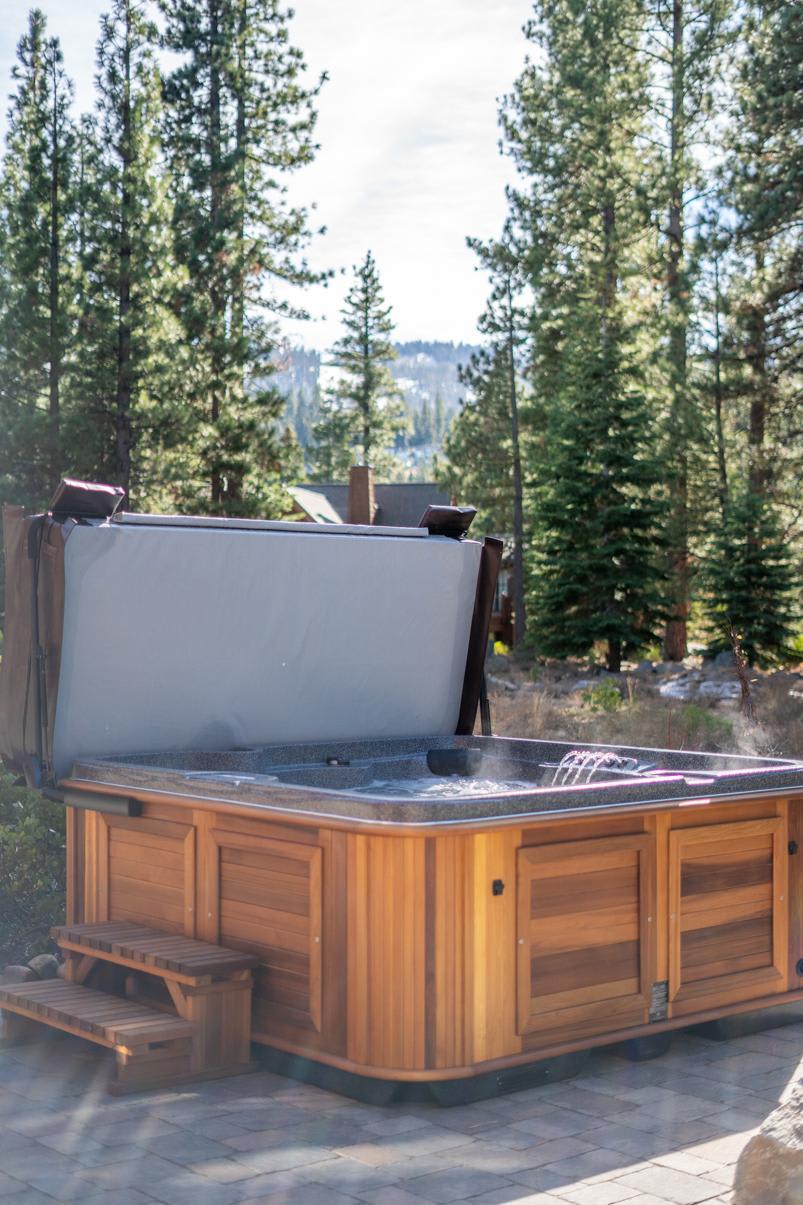 Hot tub on the patio of a Truckee vacation rental, surrounded by tall pine trees and mountain scenery.