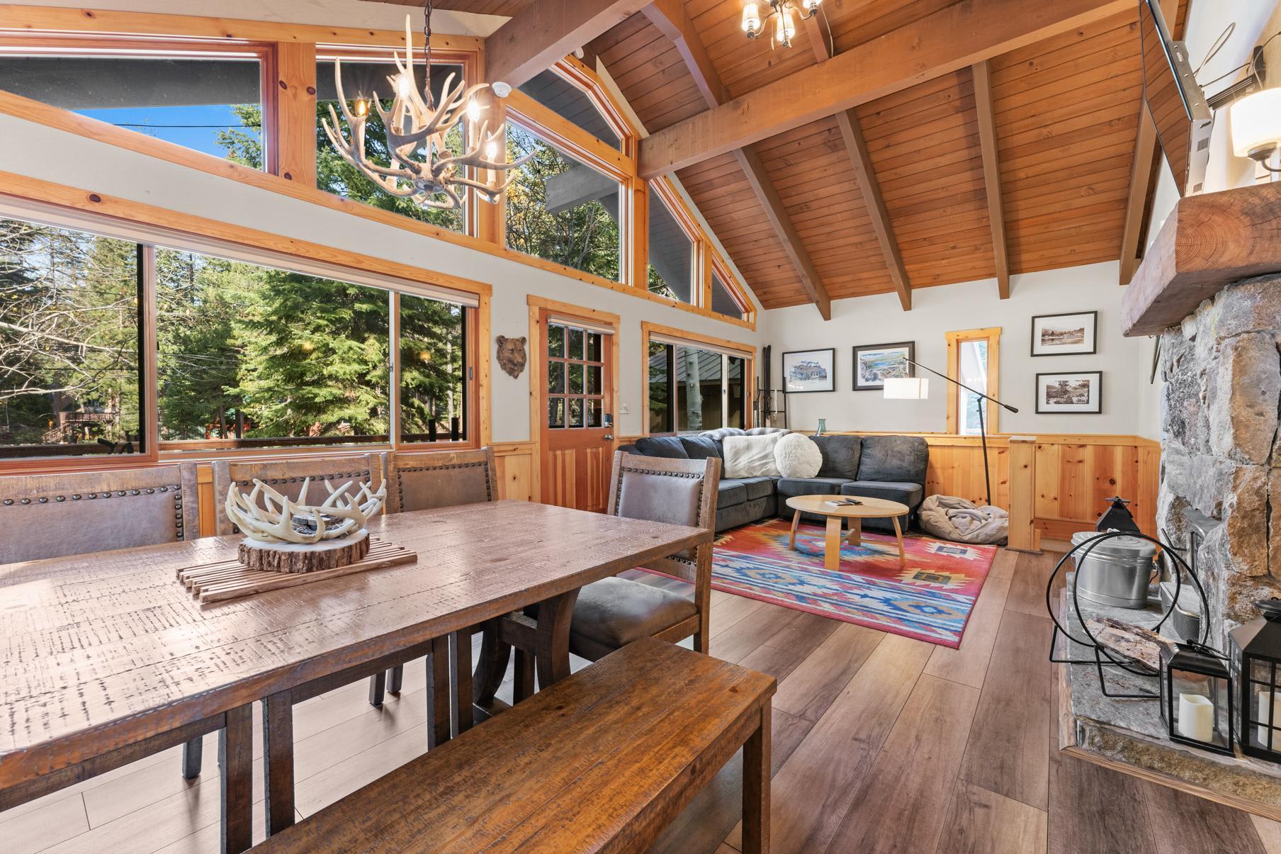 Spacious living area in a Truckee vacation rental with wood beams, large windows, antler chandelier, and cozy seating.