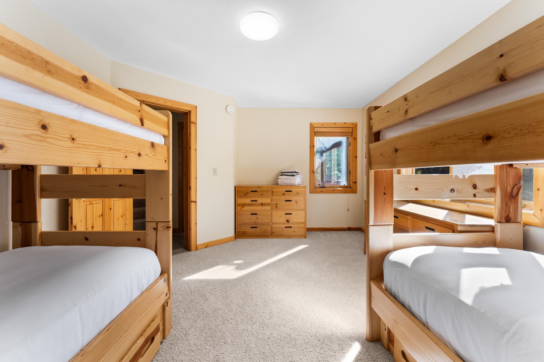 Cozy bedroom with wooden bunk beds in a Truckee vacation rental. Carpeted floor, dresser, and sunny window view.