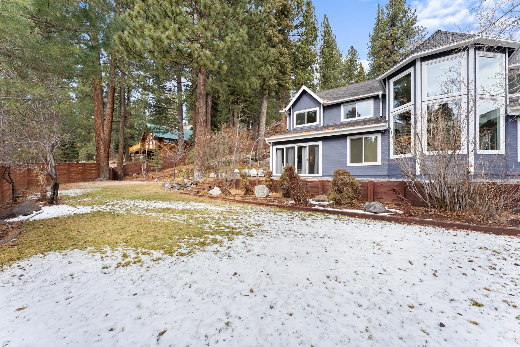 Cozy vacation rental in snowy Truckee, surrounded by tall pine trees and a spacious lawn, with a cabin-style design.