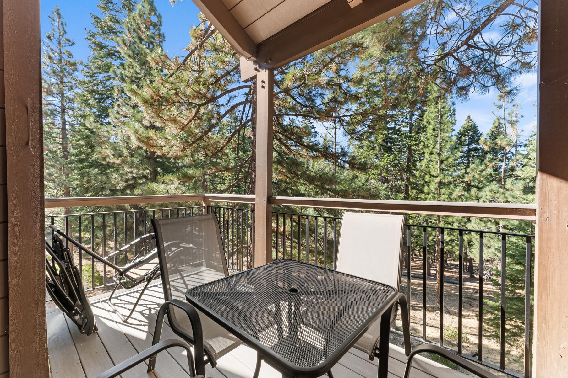 Balcony of a Truckee vacation rental with chairs and table overlooking a scenic forest landscape under a clear blue sky.