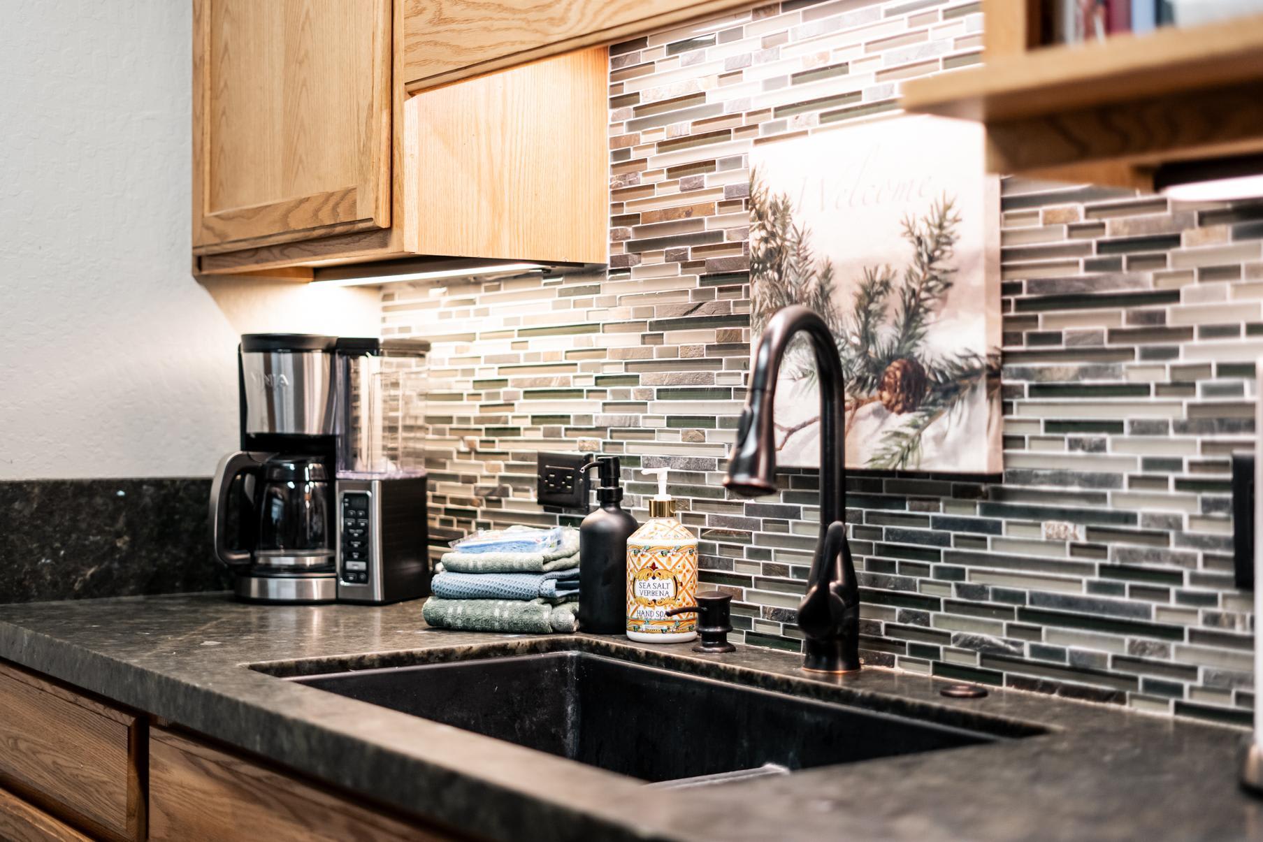 Cozy kitchen in Truckee vacation rental, featuring sleek black sink, coffee maker, and decorative mosaic tile backsplash.