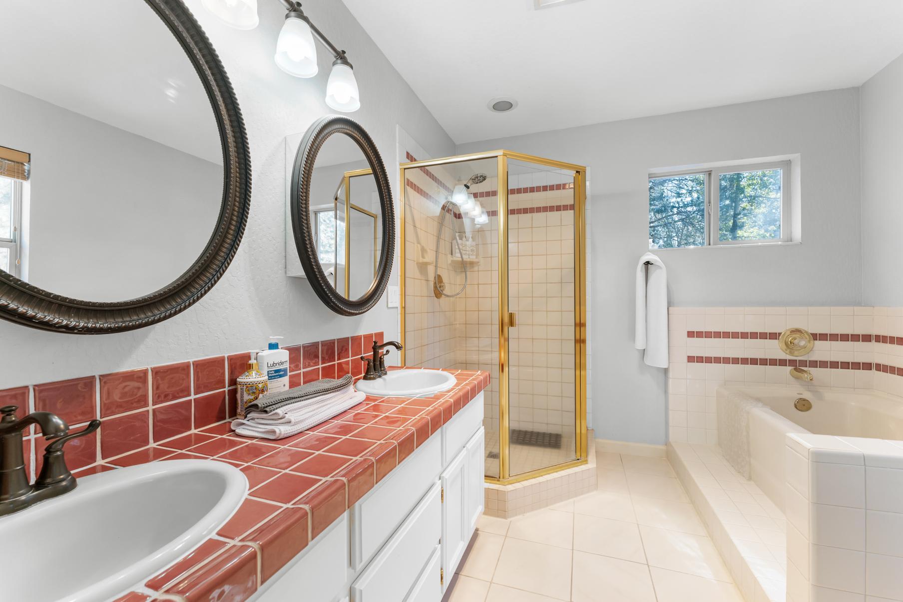 Bright bathroom in a Truckee vacation rental with double sinks, gold shower, and tub surrounded by large windows.