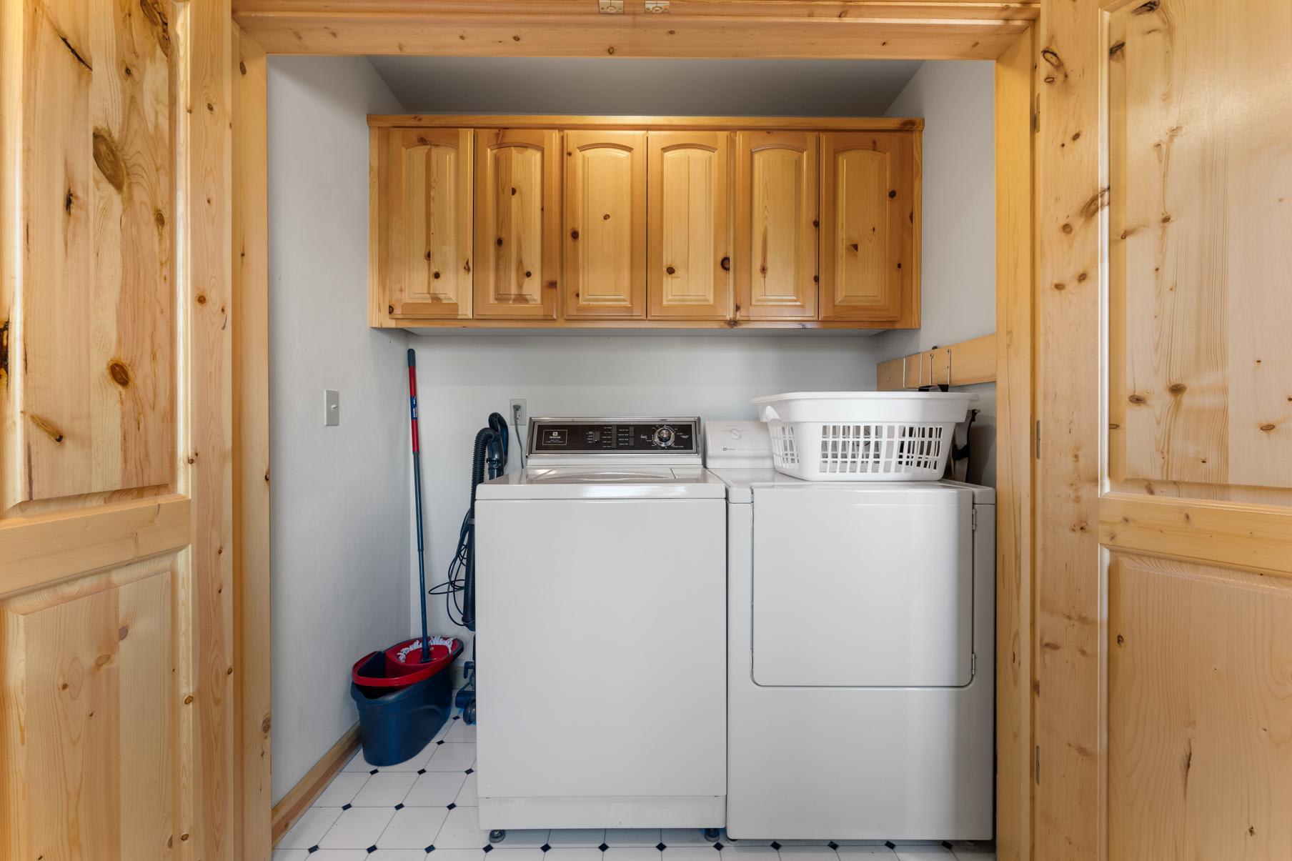 Laundry room in Truckee vacation rental with washer, dryer, wooden cabinets, and laundry basket.