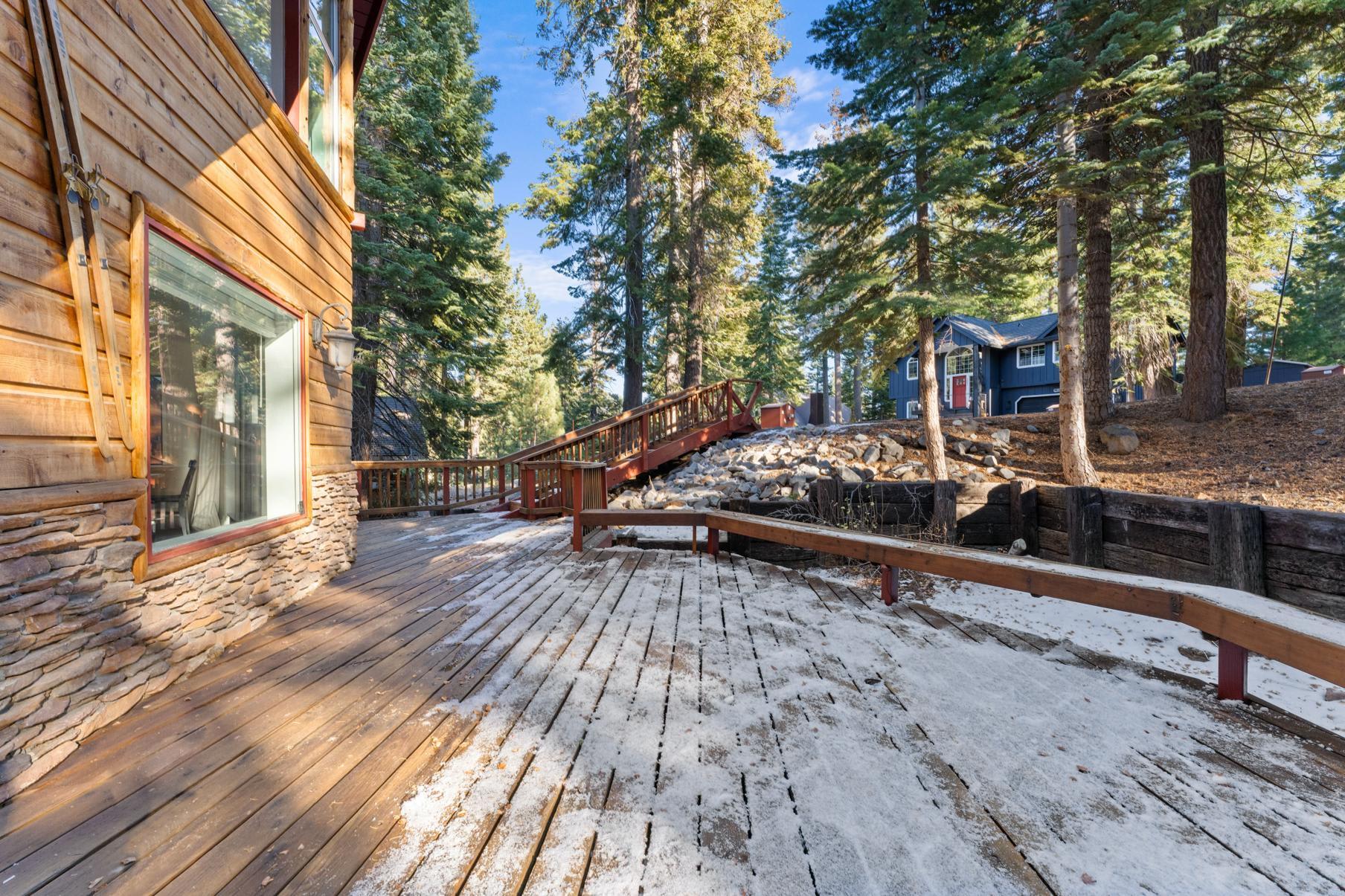 Wooden deck with light snow at a Tahoe Vista vacation rental, surrounded by trees and mountain views.