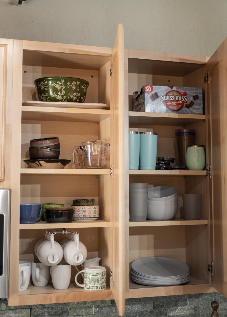 Open kitchen cabinet in a Truckee vacation rental, featuring neatly arranged dishes, mugs, and cookware.