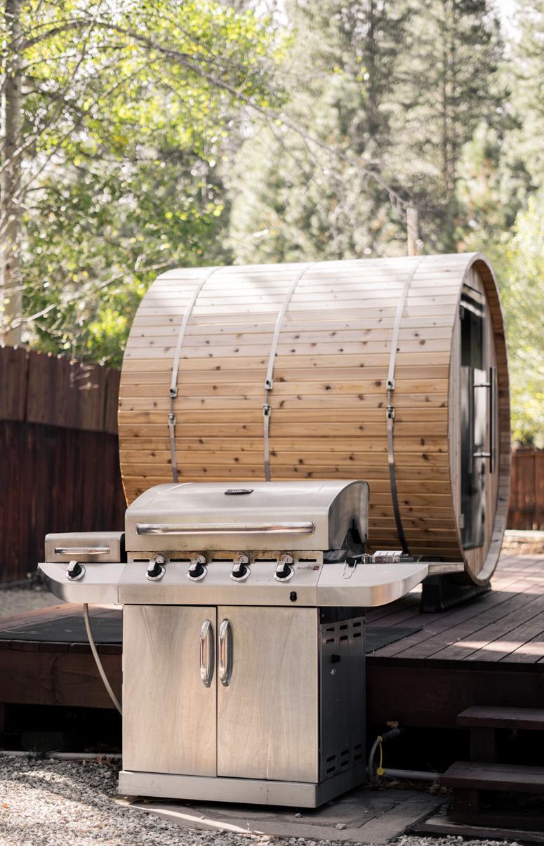 Truckee vacation rental with a barrel sauna and a stainless steel grill on a wooden deck surrounded by trees.