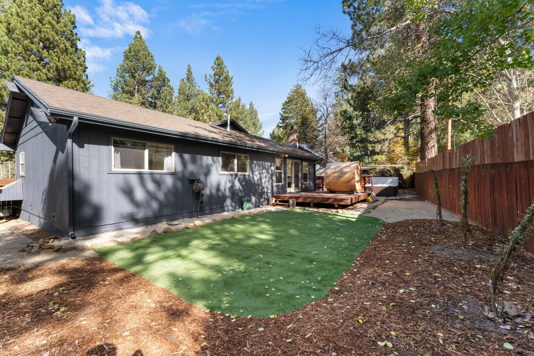 A cozy Truckee vacation rental with a wooden deck, green lawn, and surrounded by tall pine trees under a clear sky.