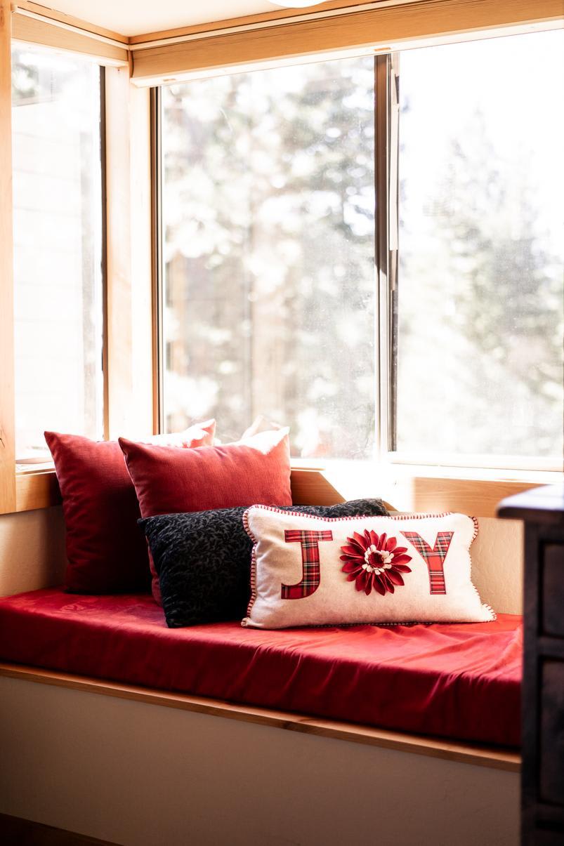 Sunny window seat with cozy pillows in a Truckee vacation rental, featuring a cushion with "JOY" in red letters.