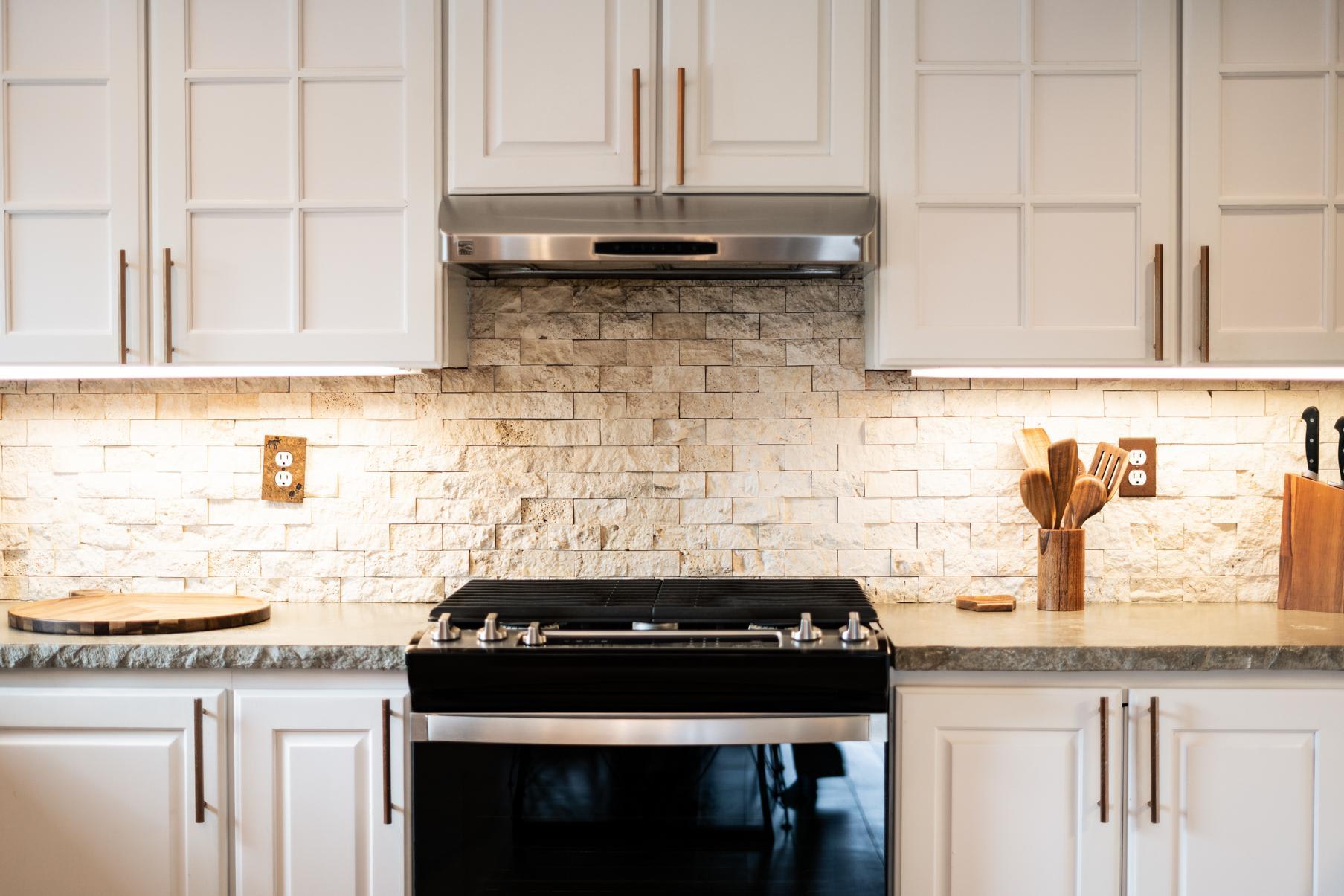 Modern kitchen in a Truckee vacation rental with white cabinets, stone backsplash, and stainless steel stove.