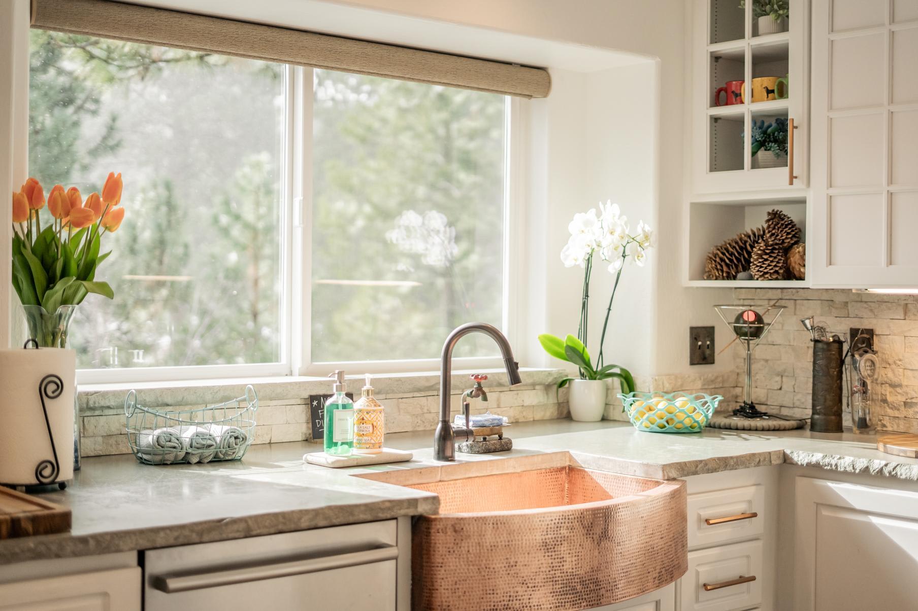 Sunlit kitchen in Truckee vacation rental, featuring a copper sink, fresh flowers, and a scenic window view.