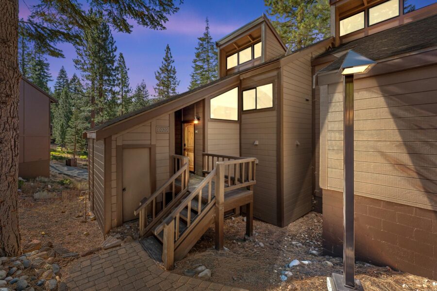 Modern cabin-style vacation rental in Truckee surrounded by tall pine trees and a wooden ramp leading to the entrance.