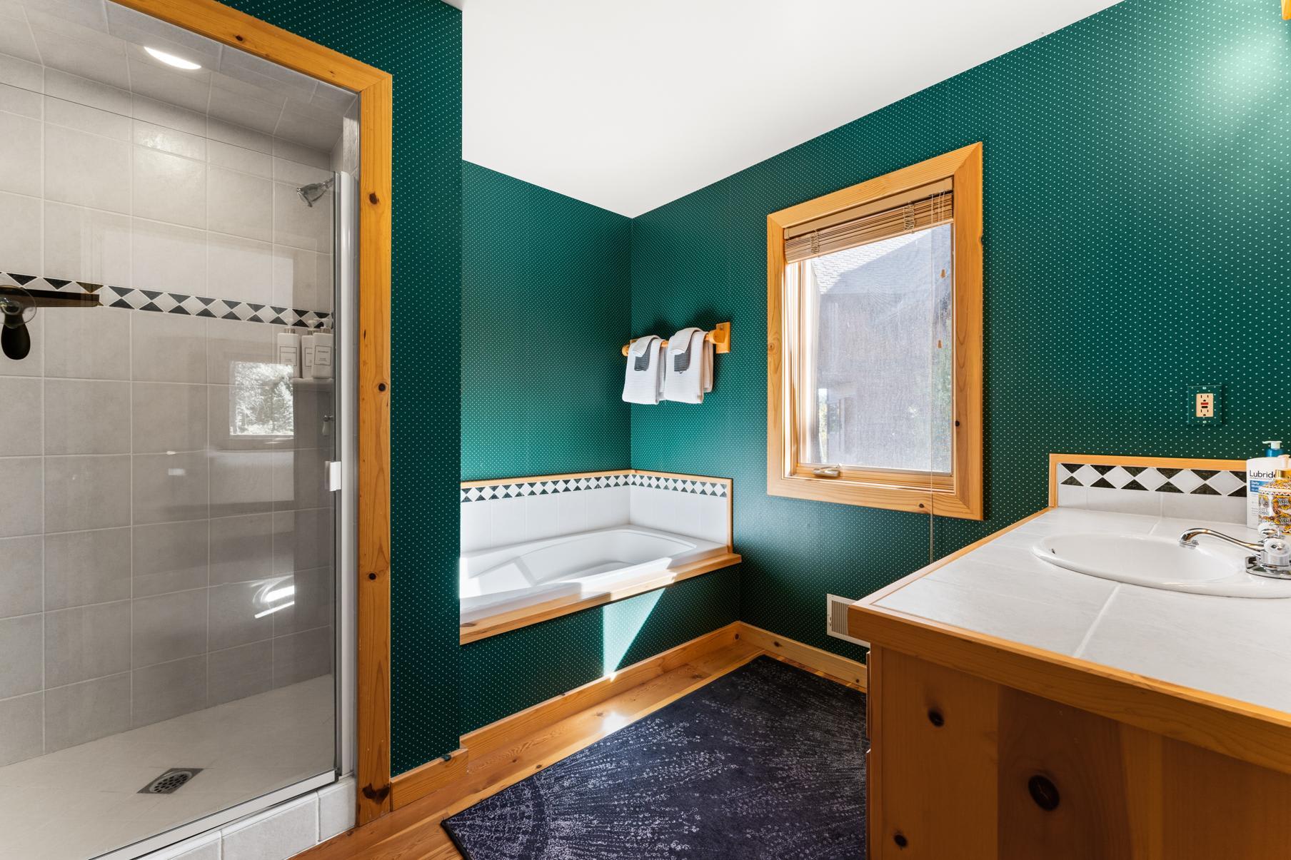 Bathroom in a Truckee vacation rental with green walls, tub, and shower. Natural wood accents and window.