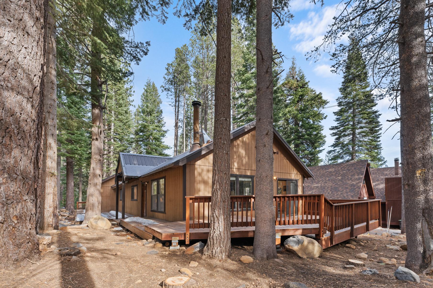 Cozy vacation rental cabin surrounded by tall pine trees in Truckee, featuring a spacious wooden deck.