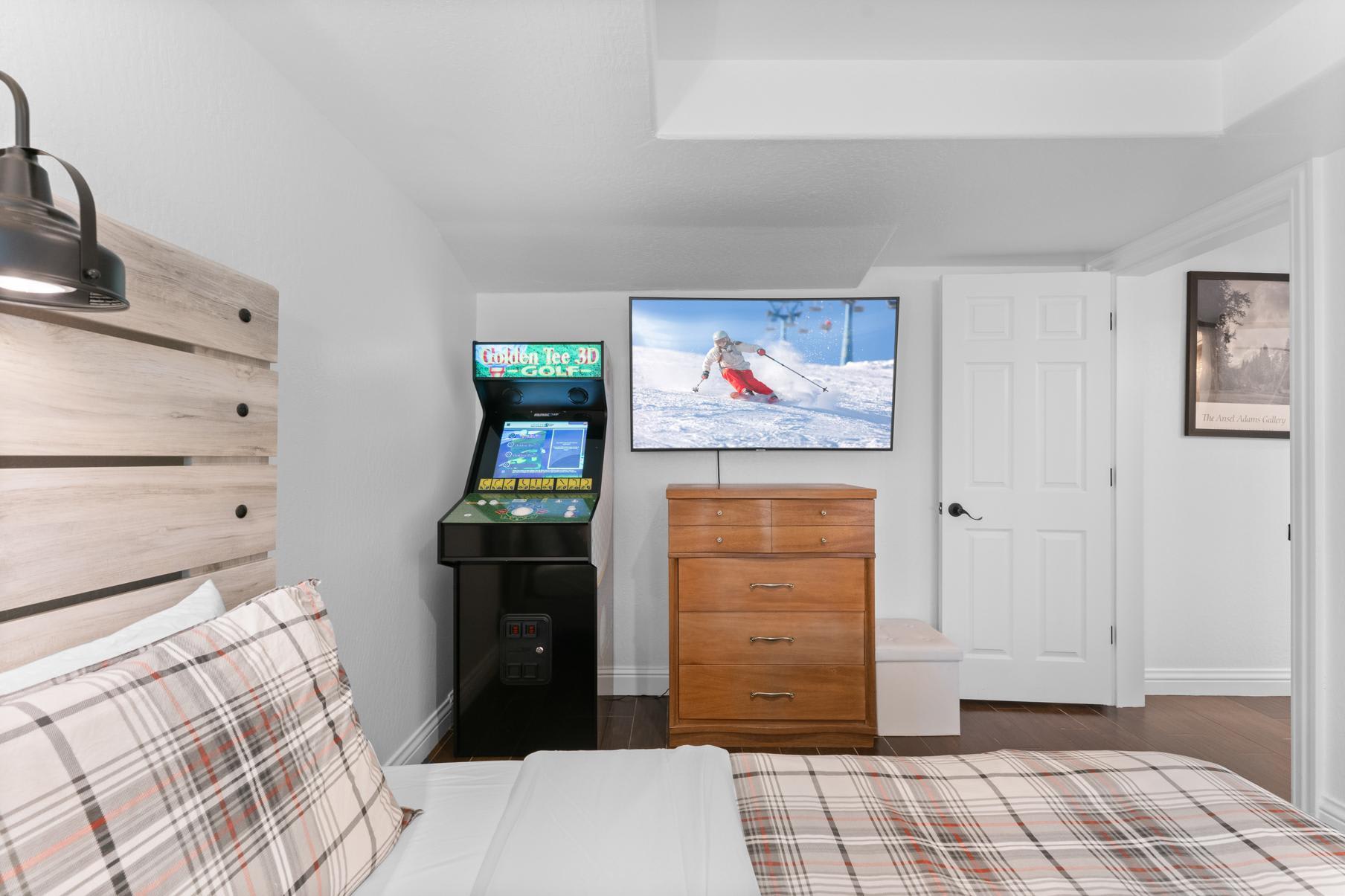 Bedroom in Truckee vacation rental, featuring a bed, arcade game, dresser, and TV showing a skier.