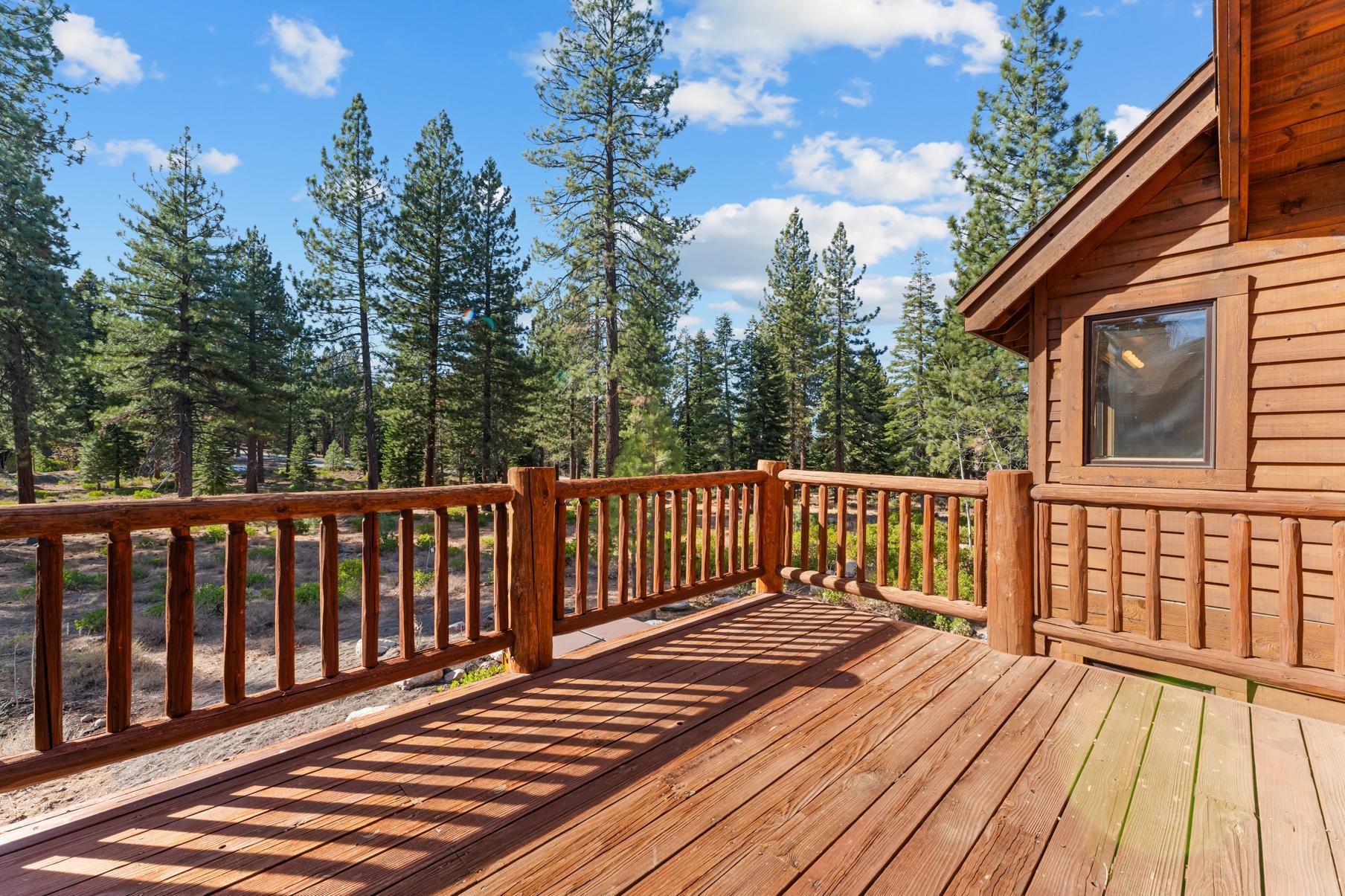 Wooden deck of a Truckee vacation rental cabin overlooking scenic pine forest under a blue sky.