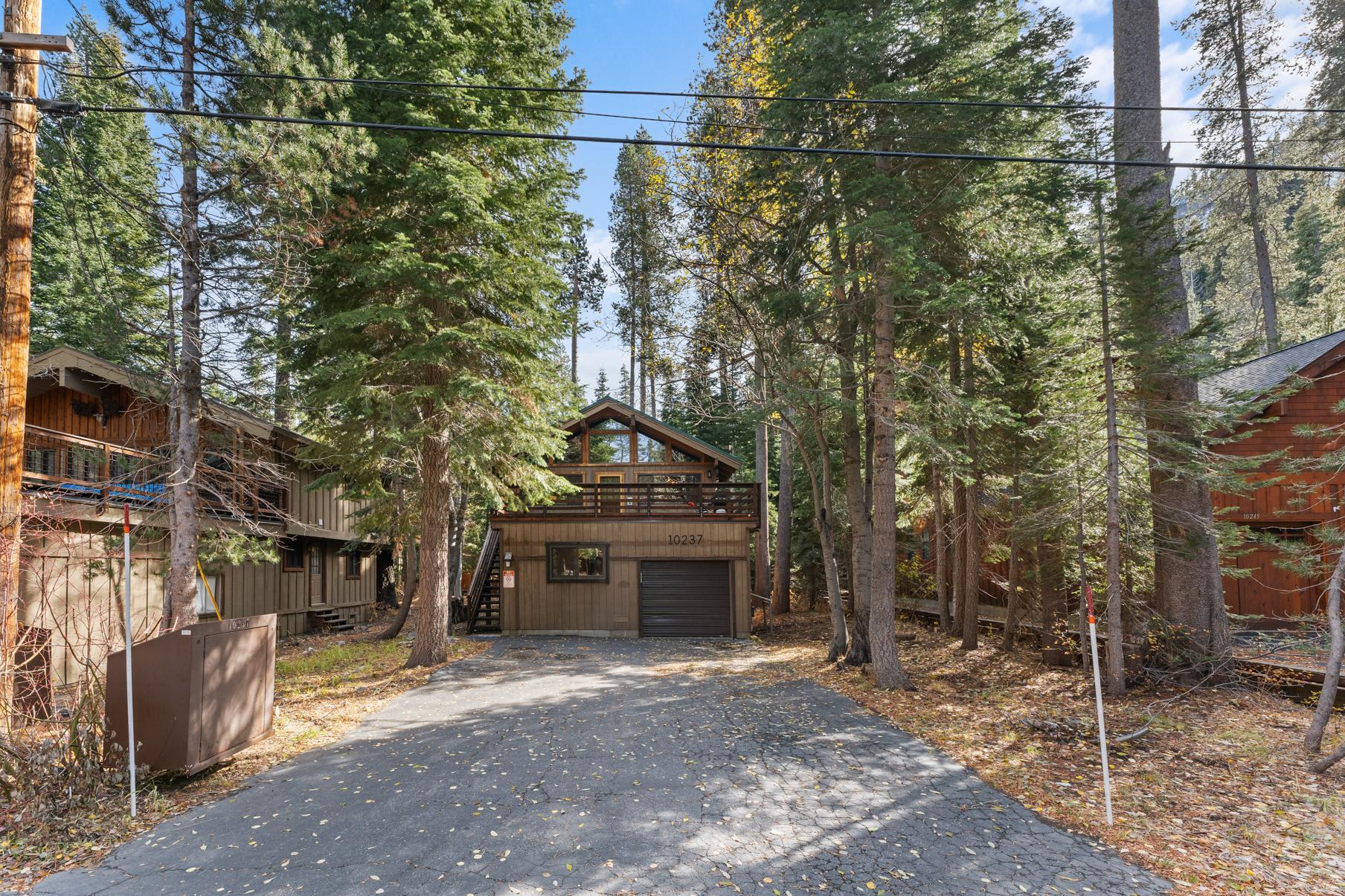 Charming cabin-style vacation rental in Truckee, surrounded by tall trees, with a driveway and wooden accents.