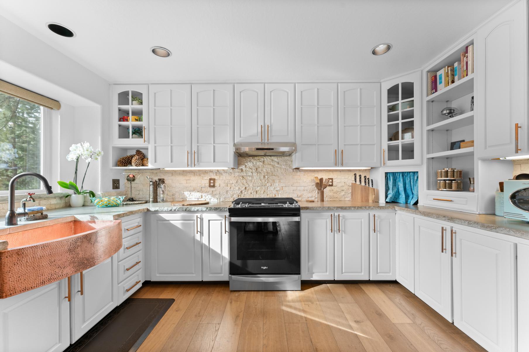 Modern kitchen in a Truckee vacation rental, featuring white cabinets, a copper sink, and hardwood floors.