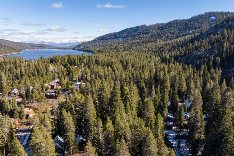 Aerial view of vacation rentals nestled in a forest near a lake in Truckee, surrounded by pine trees and mountains.