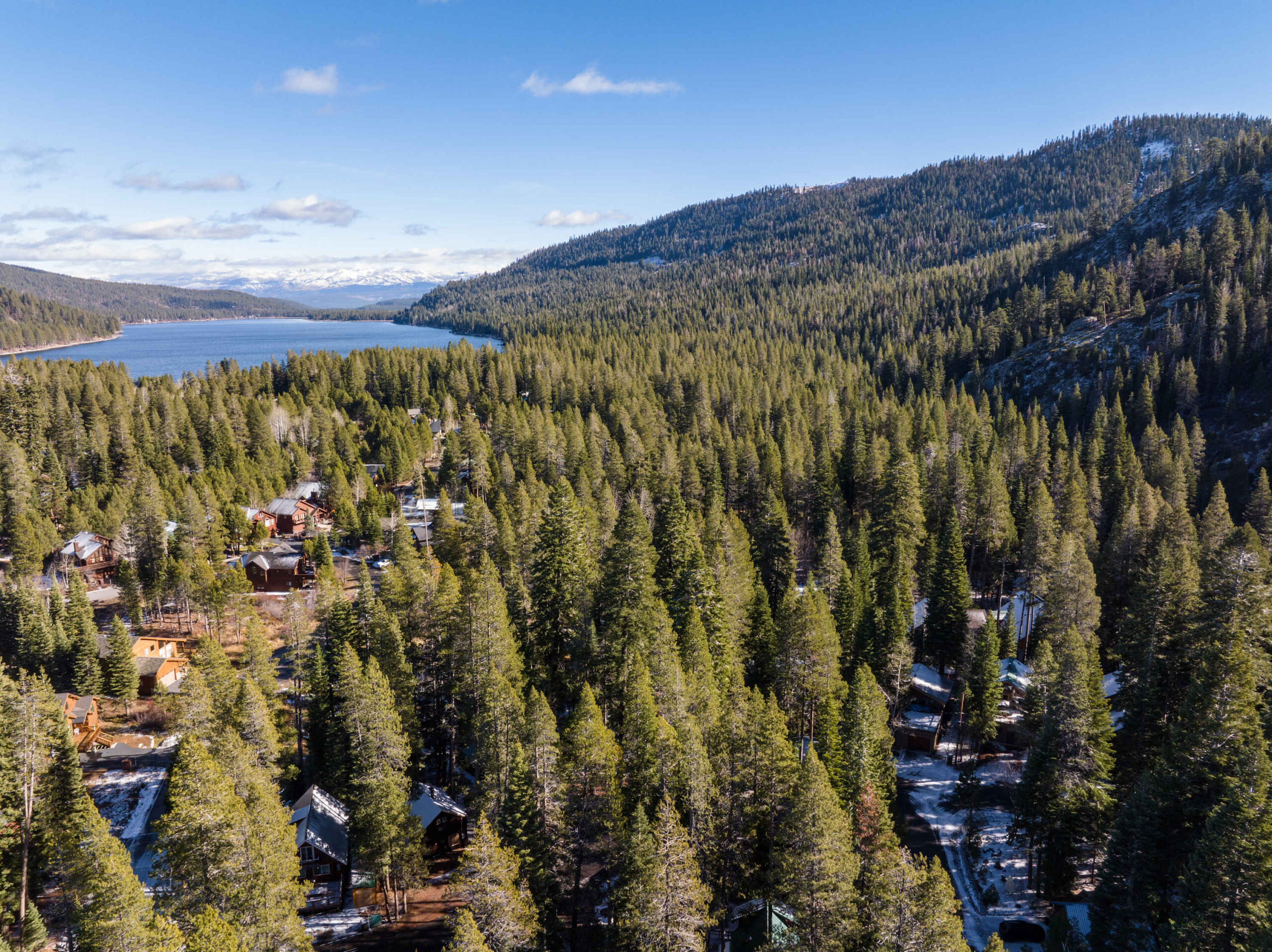 Aerial view of vacation rentals nestled in a forest near a lake in Truckee, surrounded by pine trees and mountains.