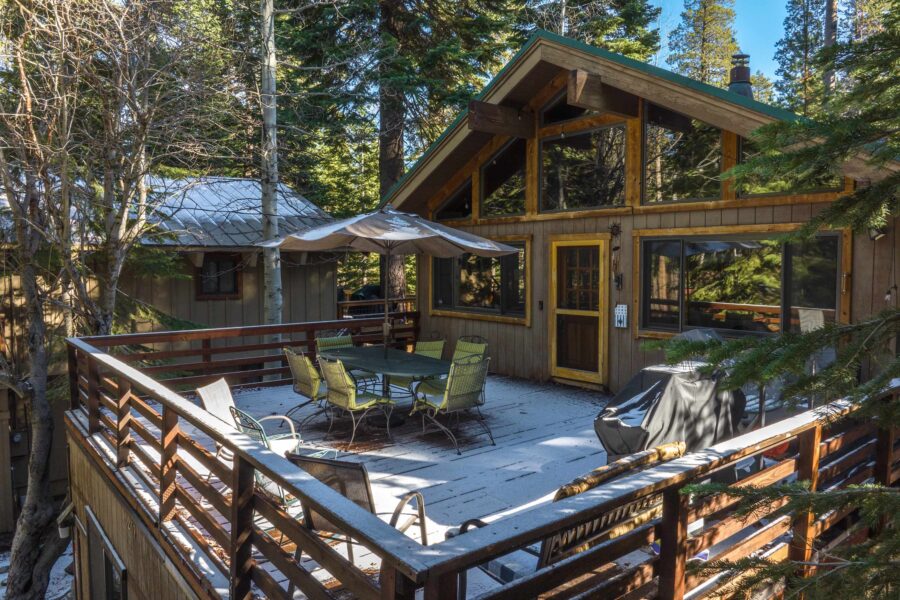 Cozy cabin vacation rental in Truckee with a snowy deck, outdoor dining set, and surrounded by lush forest trees.