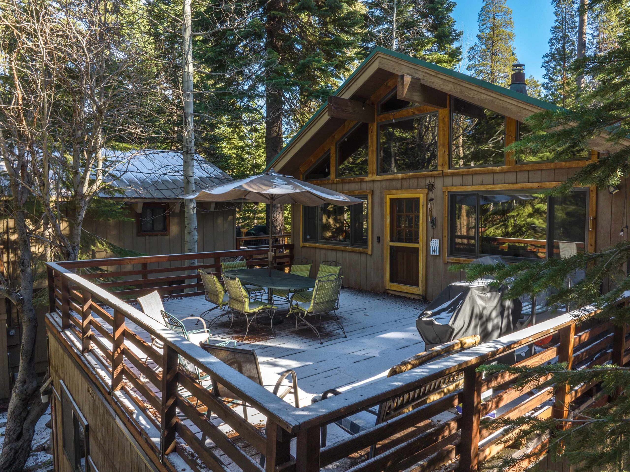 Cozy cabin vacation rental in Truckee with a snowy deck, outdoor dining set, and surrounded by lush forest trees.