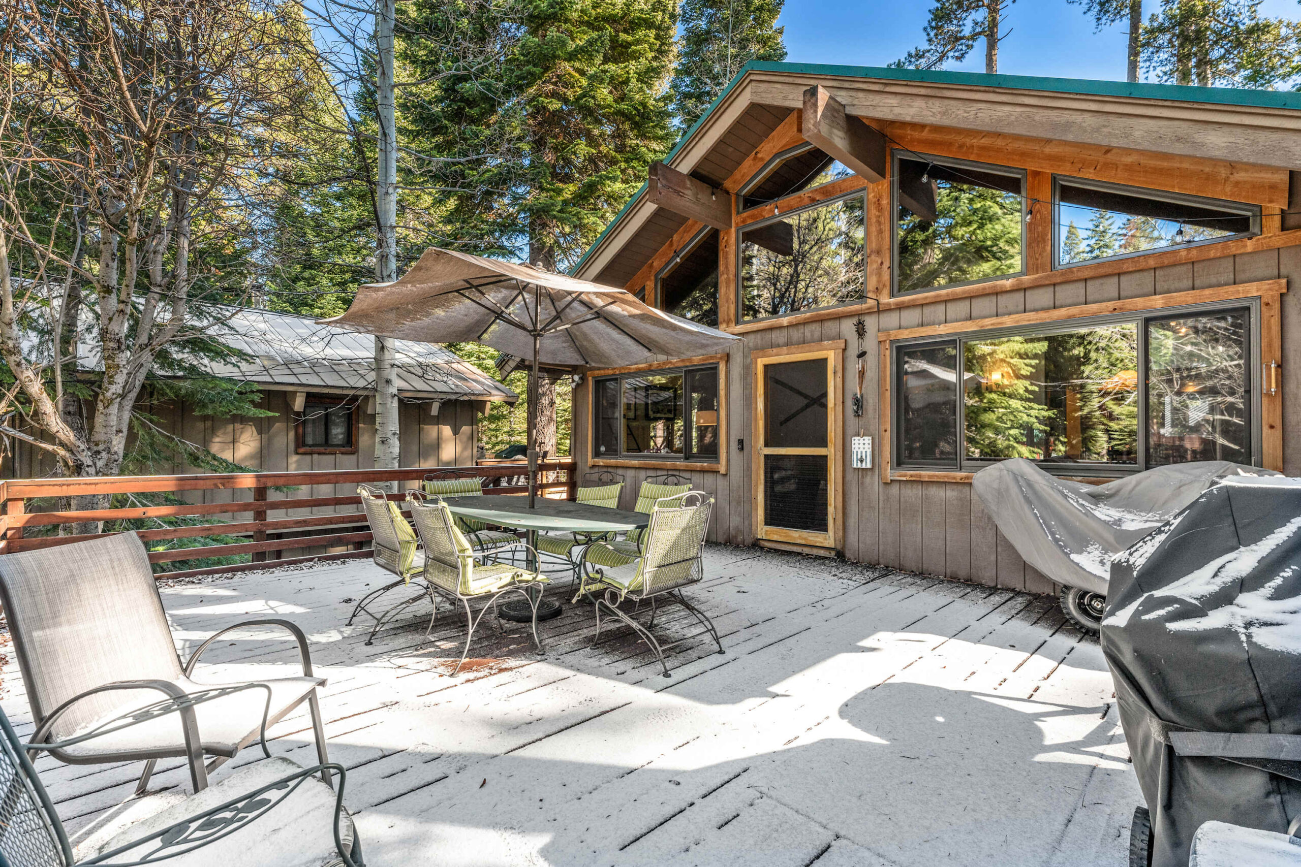 Cozy Truckee vacation rental with snowy deck, outdoor seating, and surrounded by trees.