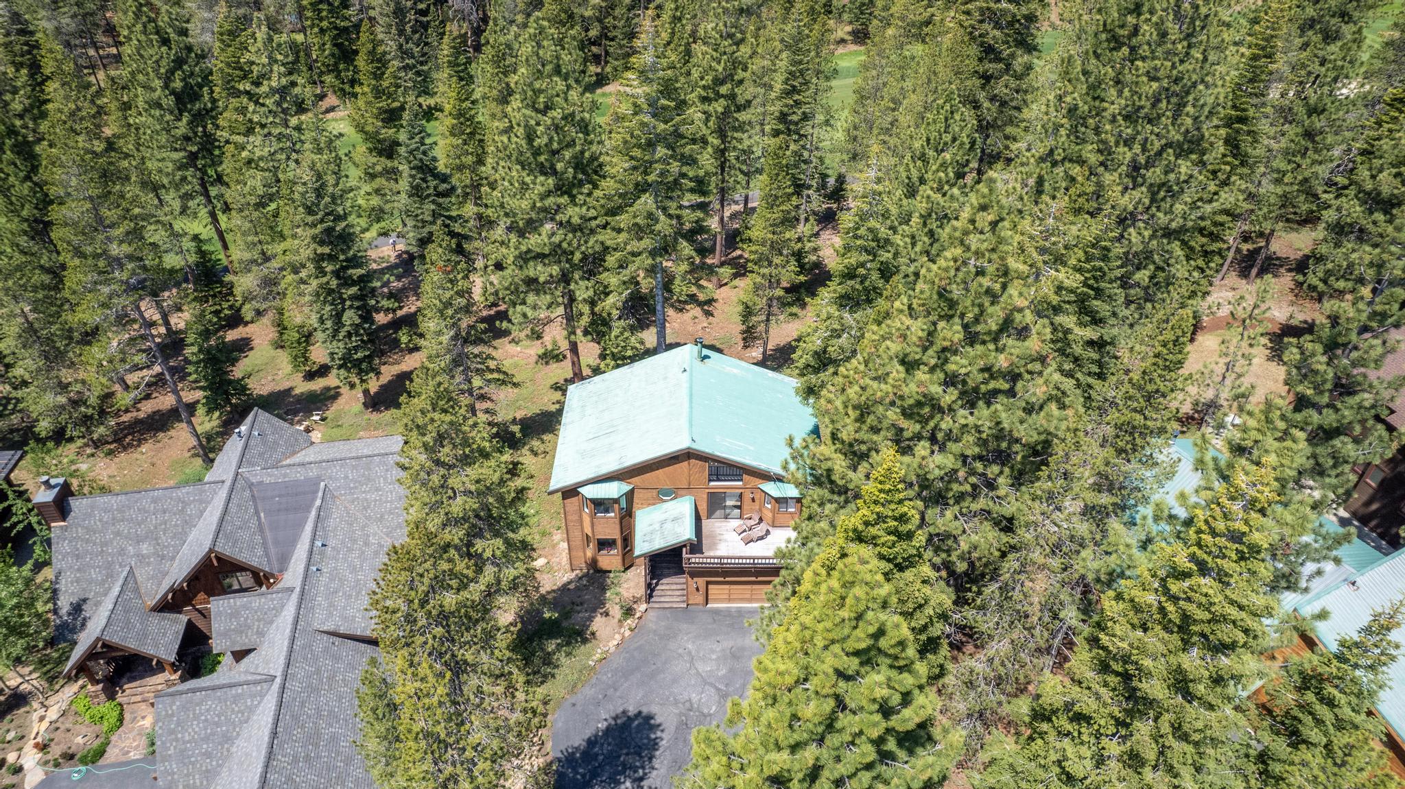 Aerial view of a secluded vacation rental nestled in a forested area in Truckee, surrounded by tall evergreen trees.