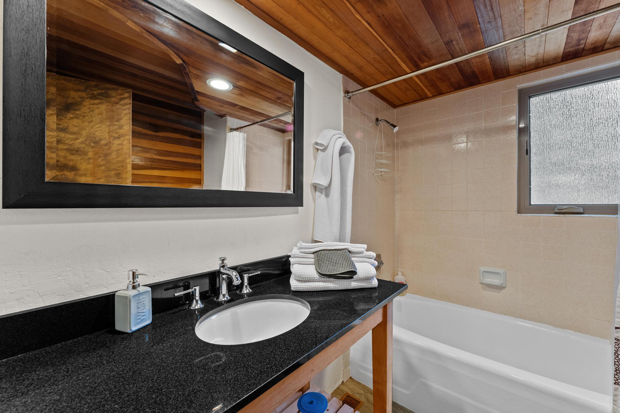 Modern bathroom in a Tahoe Vista vacation rental, featuring a sleek black countertop, wooden accents, and a cozy bathtub.